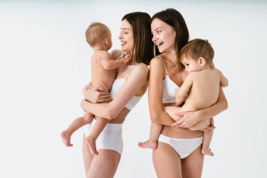 Bebeklerini renkli arka planda tutan mutlu kadınlar, küçük oğullarına bakan iç çamaşırı giyen genç kadınlar, hamilelik, annelik, insanlar ve beklenti konsepti.