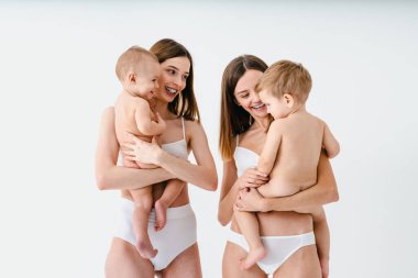 Bebeklerini renkli arka planda tutan mutlu kadınlar, küçük oğullarına bakan iç çamaşırı giyen genç kadınlar, hamilelik, annelik, insanlar ve beklenti konsepti.