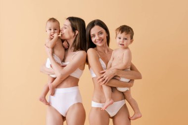 Bebeklerini renkli arka planda tutan mutlu kadınlar, küçük oğullarına bakan iç çamaşırı giyen genç kadınlar, hamilelik, annelik, insanlar ve beklenti konsepti.