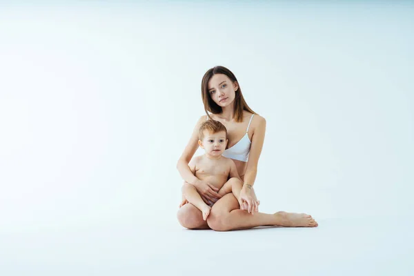 幸せな女性保持彼女の赤ちゃんに色の背景 若い女性を身に着けている下着彼女の小さな息子の世話 人々と期待の概念 — ストック写真