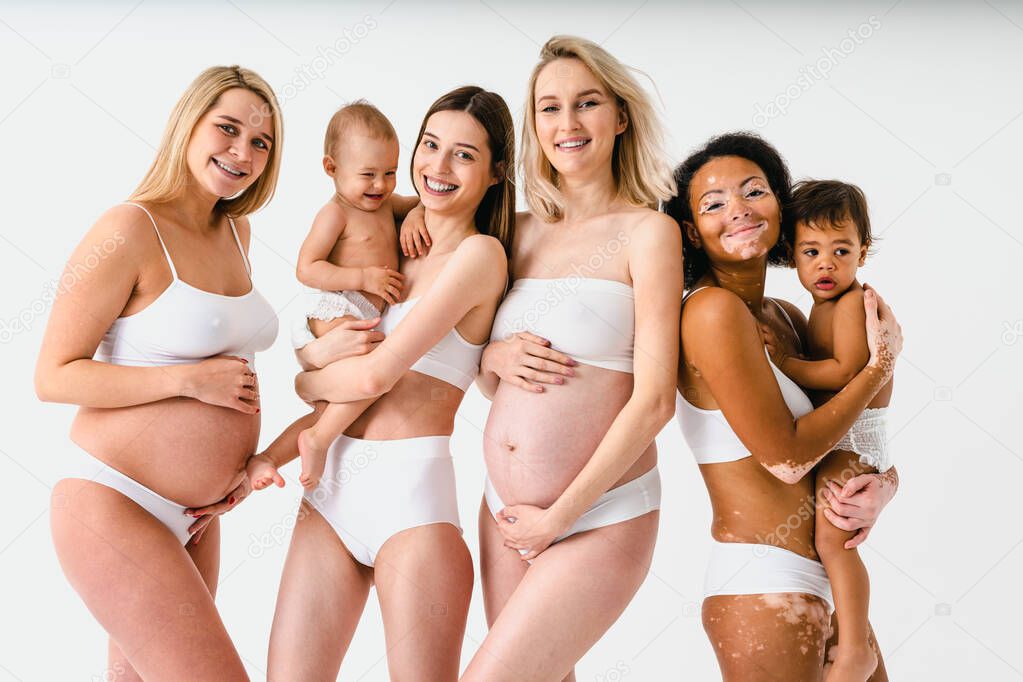 Happy pregnant women with big belly and beautiful mothers with babies in studio - Multiracial group of pregnant women and moms with childs wearing underwear - Pregnancy, motherhood, people, body positive and body acceptance concept