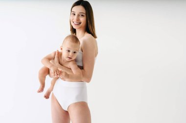 Bebeğini renkli arka planda tutan mutlu bir kadın - iç çamaşırı giyen genç bir kadın - hamilelik, annelik, insanlar ve beklenti konsepti