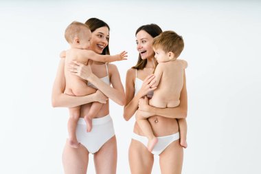 Bebeklerini renkli arka planda tutan mutlu kadınlar, küçük oğullarına bakan iç çamaşırı giyen genç kadınlar, hamilelik, annelik, insanlar ve beklenti konsepti.