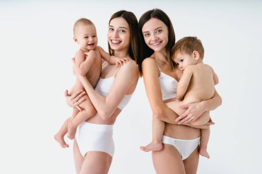 Bebeklerini renkli arka planda tutan mutlu kadınlar, küçük oğullarına bakan iç çamaşırı giyen genç kadınlar, hamilelik, annelik, insanlar ve beklenti konsepti.