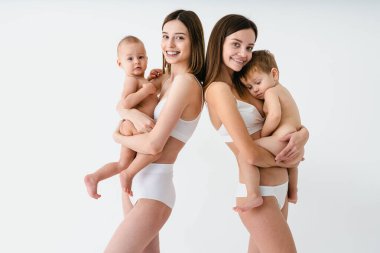 Bebeklerini renkli arka planda tutan mutlu kadınlar, küçük oğullarına bakan iç çamaşırı giyen genç kadınlar, hamilelik, annelik, insanlar ve beklenti konsepti.