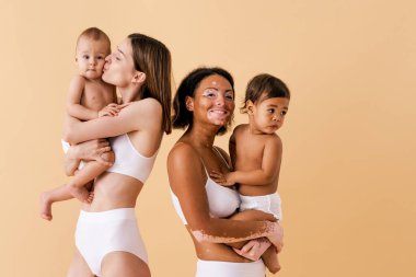 Bebeklerini renkli arka planda tutan mutlu kadınlar, küçük oğullarına bakan iç çamaşırı giyen genç kadınlar, hamilelik, annelik, insanlar ve beklenti konsepti.