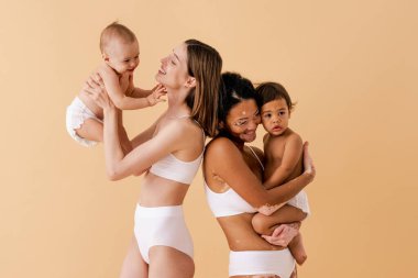 Bebeklerini renkli arka planda tutan mutlu kadınlar, küçük oğullarına bakan iç çamaşırı giyen genç kadınlar, hamilelik, annelik, insanlar ve beklenti konsepti.