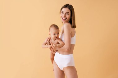 Bebeğini renkli arka planda tutan mutlu bir kadın - iç çamaşırı giyen genç bir kadın - hamilelik, annelik, insanlar ve beklenti konsepti