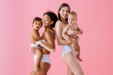 Bebeklerini renkli arka planda tutan mutlu kadınlar, küçük oğullarına bakan iç çamaşırı giyen genç kadınlar, hamilelik, annelik, insanlar ve beklenti konsepti.
