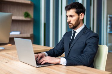 Ofisteki bilgisayar masasında oturan şık takım elbiseli bir iş adamı - Bilgisayarda çalışan yetişkin bir adam, iş ve teknoloji kavramları