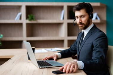 Zarif takım elbiseli bir işadamı ofiste bilgisayar masasında oturup bir video konferansına katılıyor - bir müşteri hizmetleri şirketi için internet ve dizüstü bilgisayarda çalışan yetişkin bir adam, iş, pazarlama, satış ekibi ve teknoloji konseptleri