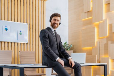 Zarif takım elbiseli bir iş adamı iş yerinde rahatlıyor. Kulaklıklı müzik dinleyen yetişkin bir adam, iş ve teknoloji konsepti.