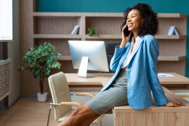 Zarif elbiseli güzel bir iş kadını bir iş stüdyosunda duruyor ve cep telefonu uygulaması kullanıyor. İş görüşmesinde Afro-Amerikan kadın portresi, iş ve teknoloji konseptleri.