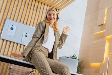 Güzel ve olgun yetişkin bir kadın ofiste duruyor, başarılı bir iş kadını portresi, zarif elbisesi olan, müzik dinleyen, şarkı söyleyen, boş zamanlarında ve işte eğlenceli anlarında.