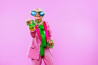 Renkli arka planda modaya uygun kıyafet portresi olan mutlu ve komik yaşlı kadın - abartılı tarzı olan genç büyükanne, yaşam tarzı, kıdemli ve yaşlı insanlar hakkında kavramlar