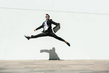 Happy and handsome adult businessman wearing elegant suit doing acrobatic trick moves in the city, alternative concept for business advertisement with energetic and creative people