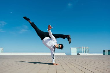 Happy and handsome adult businessman wearing elegant suit doing acrobatic trick moves in the city, alternative concept for business advertisement with energetic and creative people