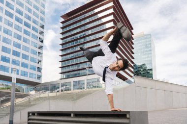Happy and handsome adult businessman wearing elegant suit doing acrobatic trick moves in the city, alternative concept for business advertisement with energetic and creative people
