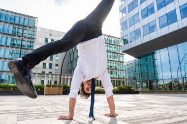 Happy and handsome adult businessman wearing elegant suit doing acrobatic trick moves in the city, alternative concept for business advertisement with energetic and creative people