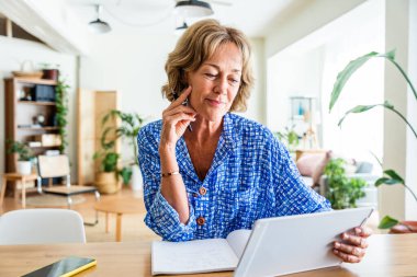 Beautiful mature senior woman at home, domestic life and leisure moments - 50-60 years old pretty female adult remote working with computer tablet