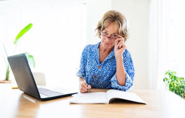 Beautiful mature senior woman at home, domestic life and leisure moments - 50-60 years old pretty female adult remote working with computer laptop