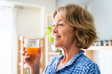 Beautiful mature senior woman at home, domestic life and leisure moments - 50-60 years old pretty female adult drinking healthy orange juice for breakfast