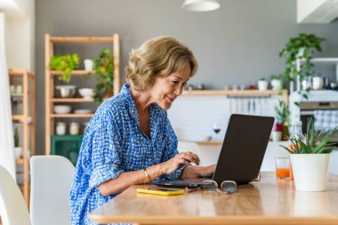 Beautiful mature senior woman at home, domestic life and leisure moments - 50-60 years old pretty female adult remote working with computer laptop