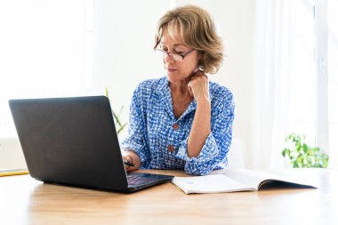 Beautiful mature senior woman at home, domestic life and leisure moments - 50-60 years old pretty female adult remote working with computer laptop