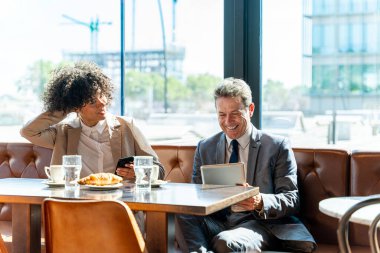 Senior businessman and beautiful hispanic businesswoman meeting in a bar restaurant  - Two colleagues bonding in a cafe after work