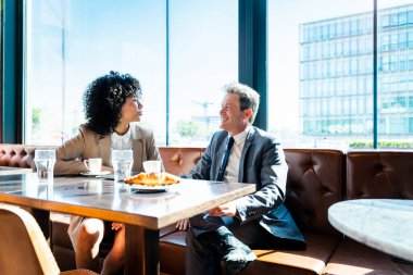 Senior businessman and beautiful hispanic businesswoman meeting in a bar restaurant  - Two colleagues bonding in a cafe after work