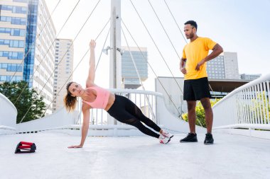 Açık havada ırklar arası spor eğitimi alan çift spor giyer ve vücut kaslarını, karın kaslarını, dayanıklılığı ve kardiyo gücünü arttırmak için dışarıda egzersiz yapar.