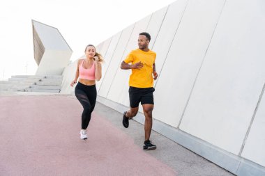 Açık havada koşan ırklar arası spor bir çift spor giyer ve vücut kaslarını, karın kaslarını, dayanıklılığı ve kardiyo gücünü arttırmak için dışarıda egzersiz yapar.