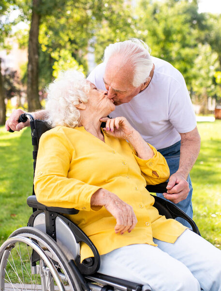 Beautiful senior couple with disability outdoors - Old people in the age of 60, 70, 80 having fun and spending time together, concepts about elderly, seniority, healthcare and wellness aging