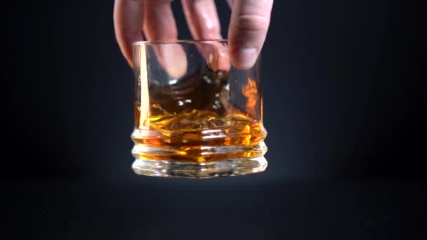 Geschäftsmann im Besitz von Whisky, einem Restaurant Luxus-Whisky. Mann rührt langsam goldenen Whisky in das Glas mit Eis vor Holzgrund. Scotch im Becher. Bourbon im Highball. Zeitlupe. Nahaufnahme — Stockvideo