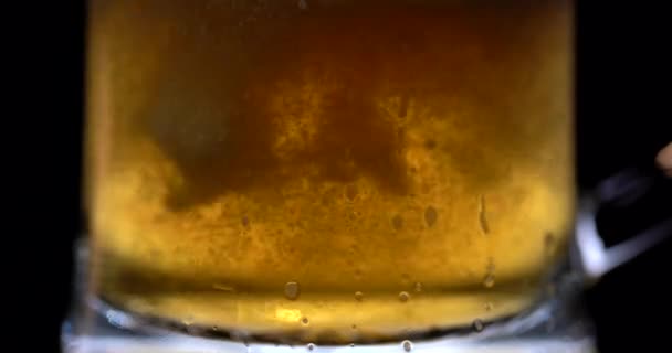 Light cold beer pours into a wet glass. With bubbles and foam. Black background. Beer pouring. Alcohol concept. Before holiday. Low angle shot. Close up. Cold Light Beer in a glass with water drops — Stock Video