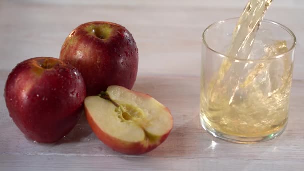 Крупный план сока наливают в стакан на столе в саду рядом со свежими яблоками. На естественном зеленом фоне. Концепция здорового питания. — стоковое видео