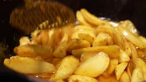 Volteando las papas doradas asadas especiadas con aceite, sal y pimienta negra en una bandeja para hornear. Proceso de cocción de patatas asadas al horno perfectas. Vista macro — Vídeos de Stock