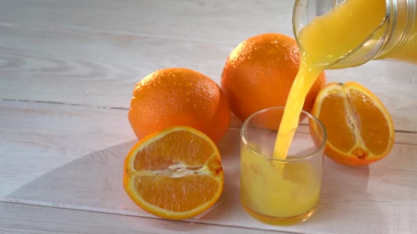 Orangensaft wird ins Glas gegossen. In Zeitlupe wird frischer Orangensaft in die weiße Tischoberfläche geschüttet. Viele frische Säfte. Saft in Scheiben geschnitten. Gesundes und frisches Getränk für den Sommertag — Stockvideo