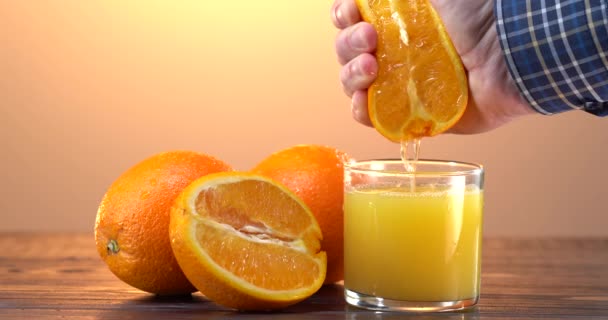 La mano del hombre exprime el jugo de la naranja fresca. Muchas naranjas en rodajas sobre la mesa. Vaso con bebida recién exprimida. Concepto sobrio y cuidado. — Vídeo de stock