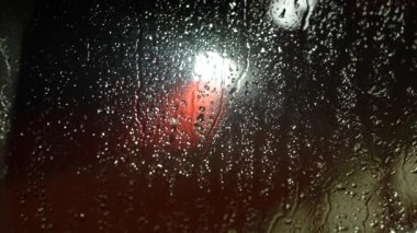 Pencereye kar damlıyor. Arka planda kırmızı ve beyaz ışıklar var. Kış mevsimi