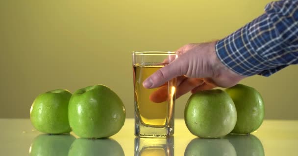 Мужчина в клетчатой рубашке берет яблочный сок со стеклянного стола. Мужская рука берет стакан со многими свежими яблоками с поверхности стекла. Желтый цвет фона. Концепция здорового питания. — стоковое видео