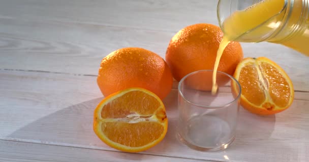 Bardaklara taze portakal suyu dök. Beyaz ahşap masa. Yüzeyde bir sürü portakal var. Sağlıklı bir içki. Yönlendirme atışı. Reklamcılık. — Stok video
