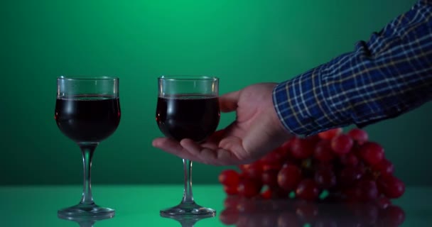 Alcohol. Two glasses with red vine and grape on the reflected surface. Green Background. Man hand takes one glass. Friday evening concept. Tasty drink. Advert shot — Stock Video