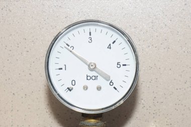 Manometer instrument with white dial on wall of brown ceramic tiles. Industrial concept