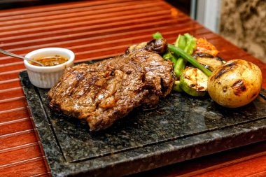 Ahşap bir tahtanın üzerinde sebzeli ızgara biftek ve sos.