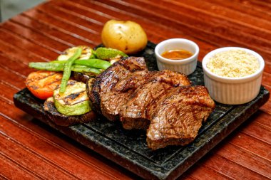 Sebzeli ızgara biftek ve ahşap bir tahtanın üstünde sos.