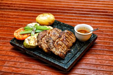 Ahşap bir tahtanın üzerinde sebzeli ızgara biftek ve sos.