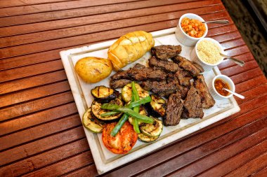 Ahşap bir masada ızgara domuz pirzolası, sebze ve sos.