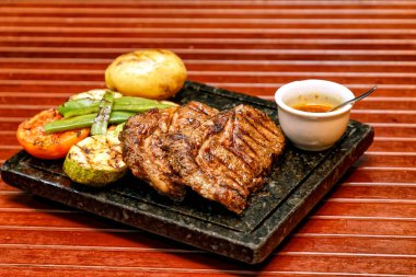 Sebzeli ızgara biftek ve ahşap arka planda baharatlar.