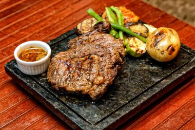 Sebzeli ızgara biftek ve ahşap arka planda baharatlar.